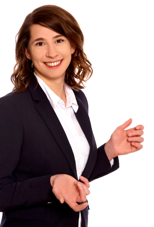 Eine lächelnde Frau in einem dunklen Blazer und weißem Hemd gestikuliert mit einer Hand, während sie die andere Hand an der Taille hält.